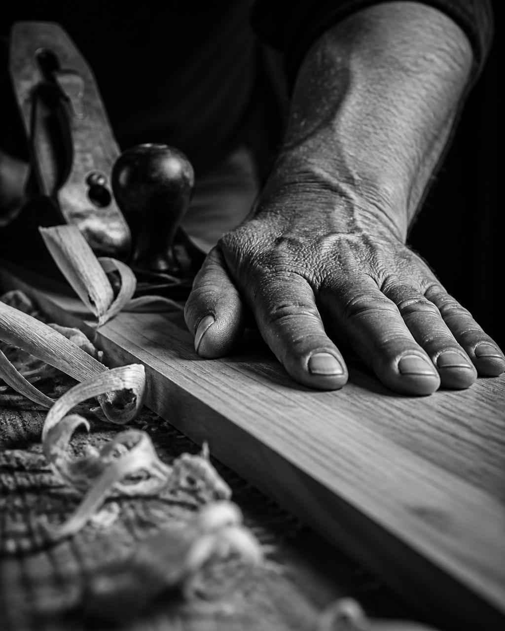 A craftsman's hand resting on a freshly planed wood board